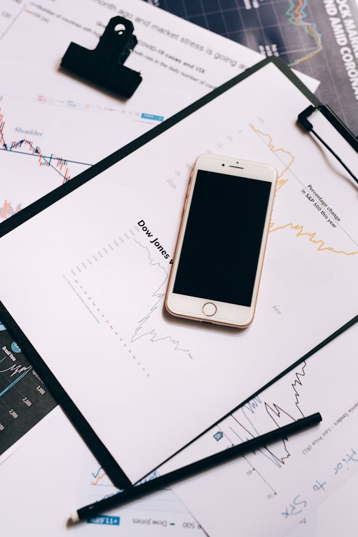 Smartphone resting on financial charts and clipboard, depicting stock market analysis.