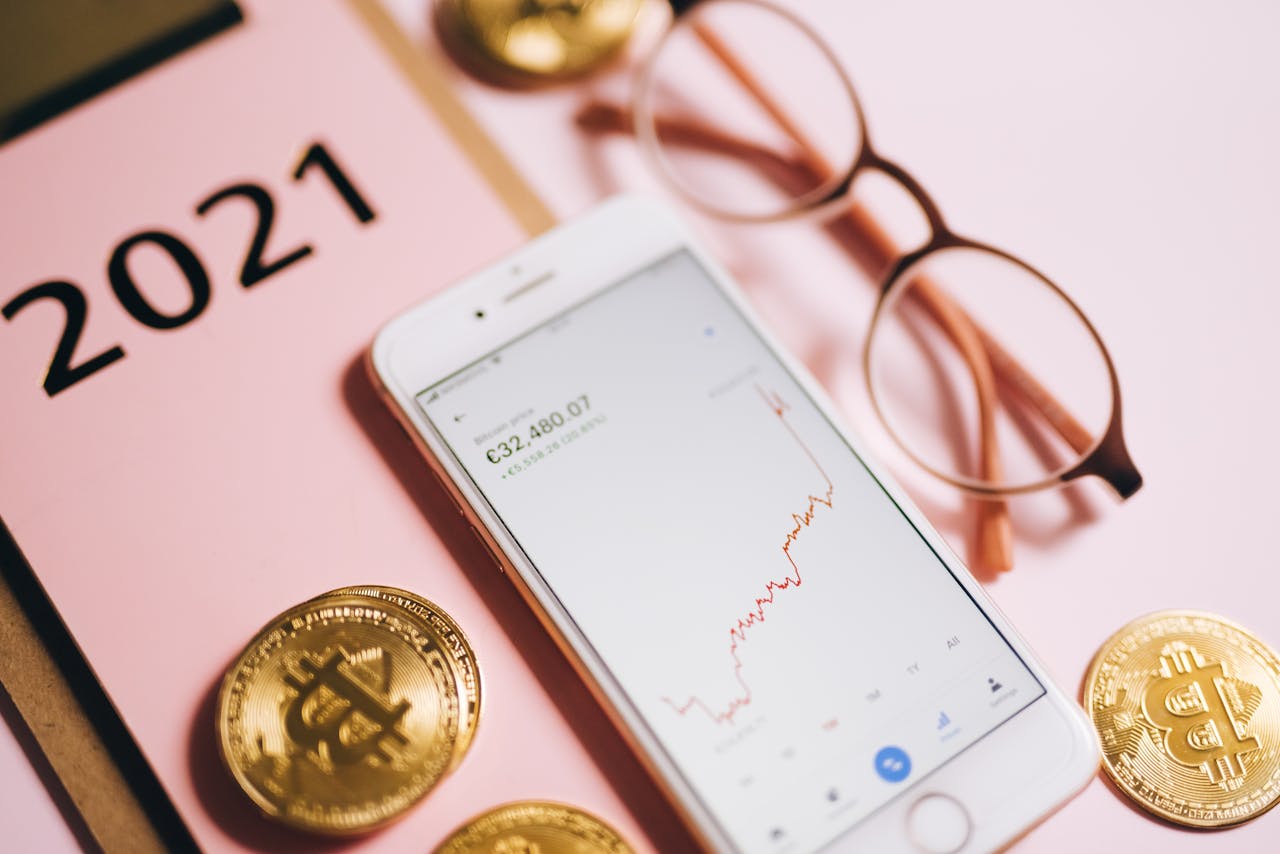 Smartphone displaying financial chart with Bitcoin coins on pink background.